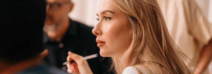 Woman holding a pen and listening attentively during a meeting, with colleagues blurred in the background