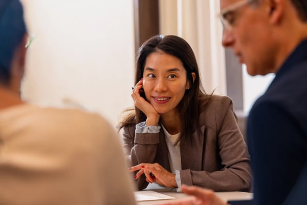 Woman smiling and resting her head on her hand while talking with colleagues.
