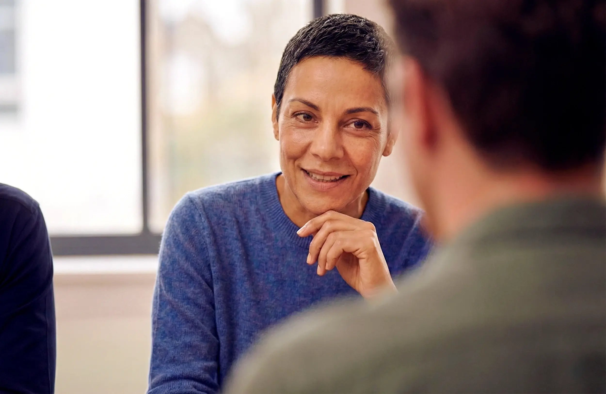 Woman smiling and resting her chin on her hand while talking in a meeting.