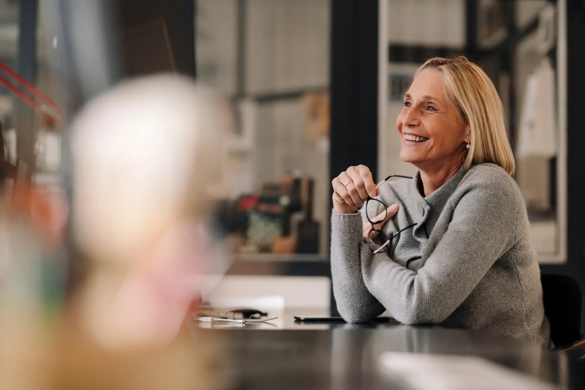 Woman smiling and holding her glasses while listening at a meeting.