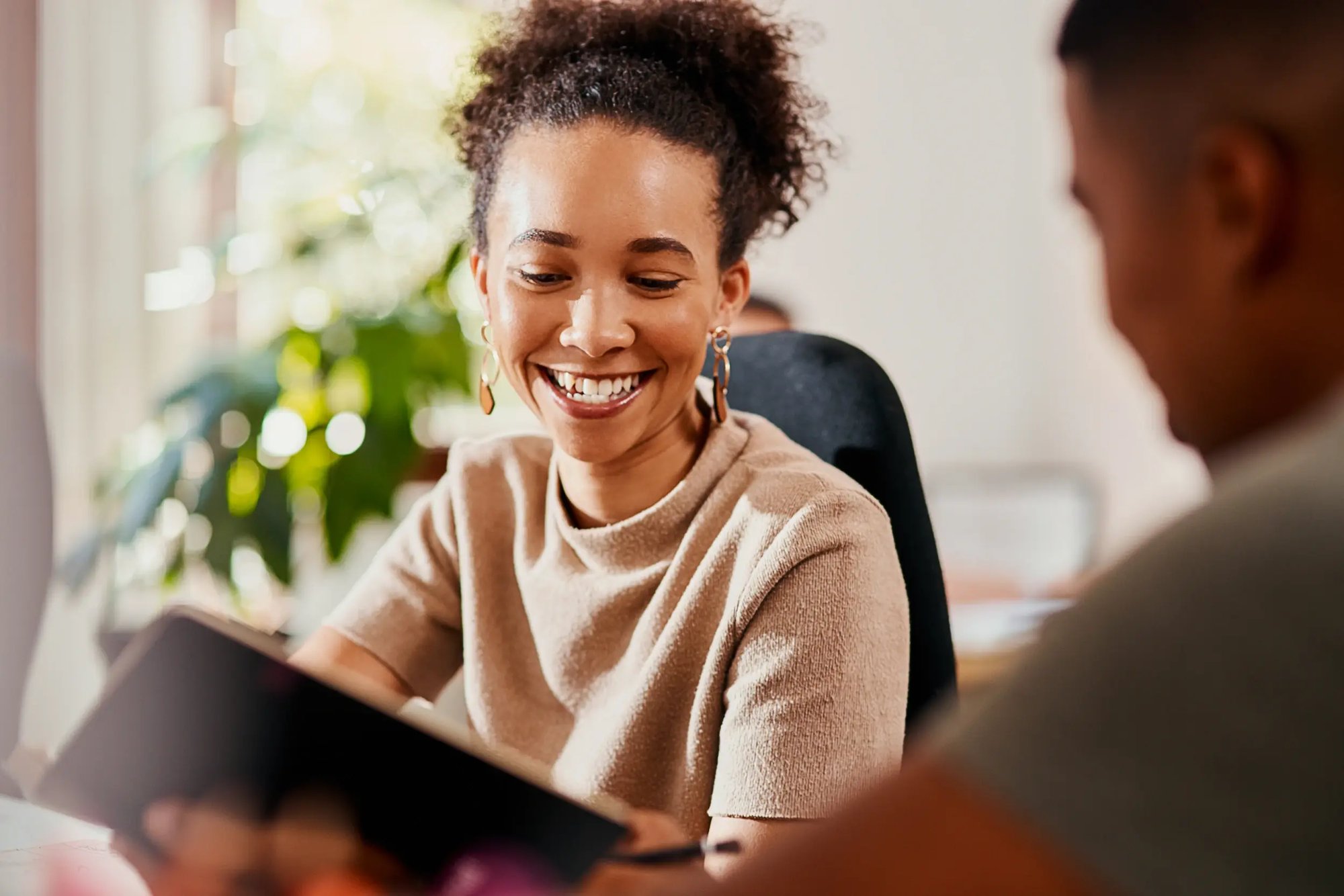 Woman smiling while looking at a tablet during a meeting.