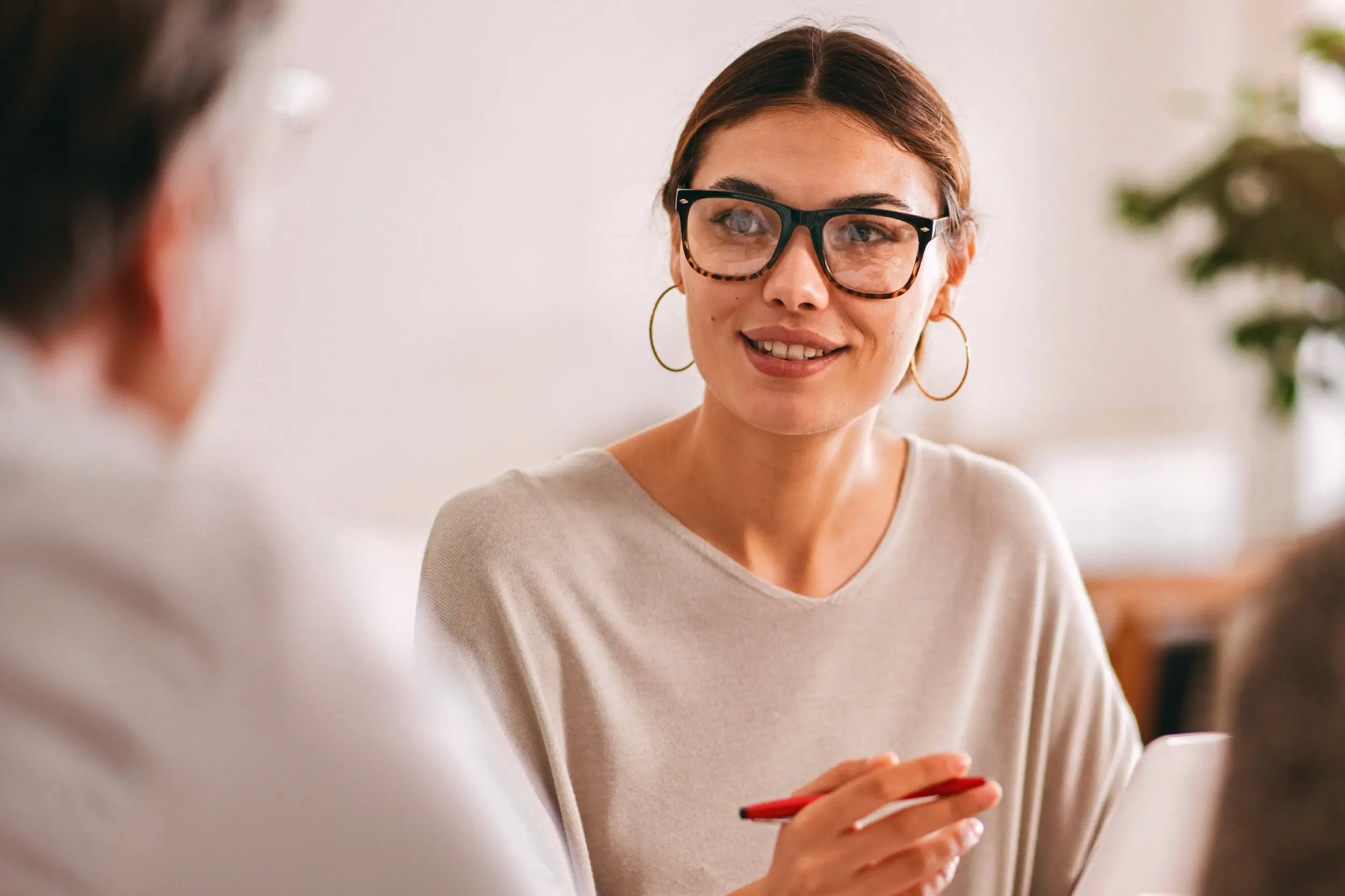 Woman wearing glasses speaking and holding a pen during a meeting.